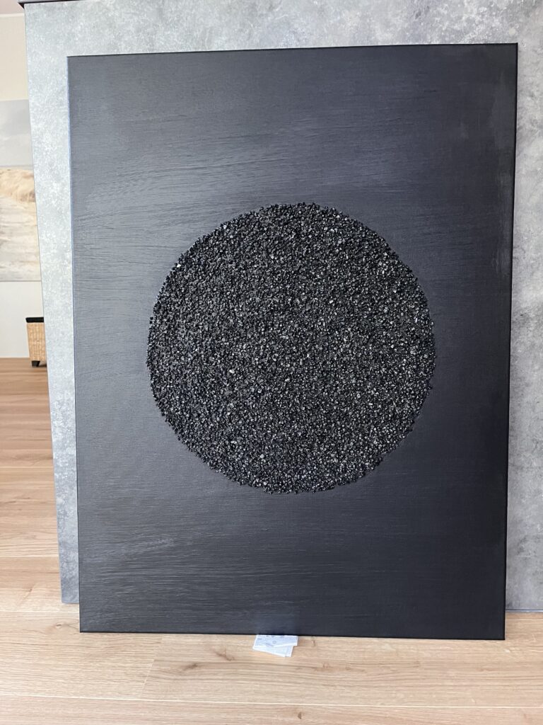 Mustal taustal struktuurmaal Kuukivi, kus sätendavad kivikesed on paigutatud keskele suurde ringi, sümboliseerides kosmilist energiat.