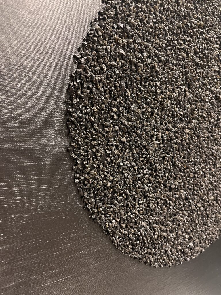 Mustal taustal struktuurmaal Kuukivi, kus sätendavad kivikesed on paigutatud keskele suurde ringi, sümboliseerides kosmilist energiat.